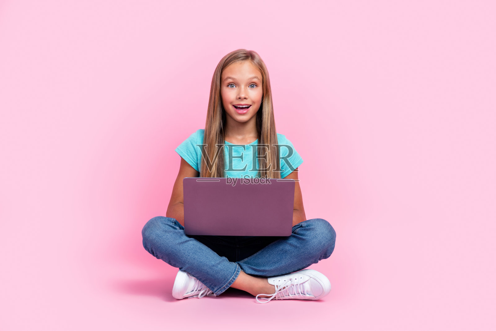 全身照，惊讶的小孩穿着青绿色T恤，正在打字，手中拿着苹果或三星的现代设备，背景为粉色。照片摄影图片