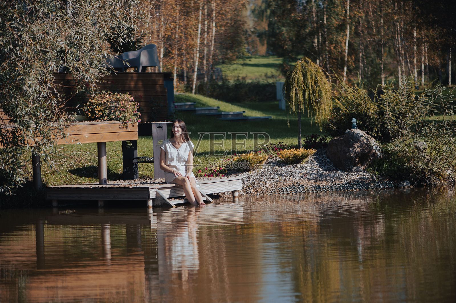秋天，女人坐在池塘边的码头上照片摄影图片