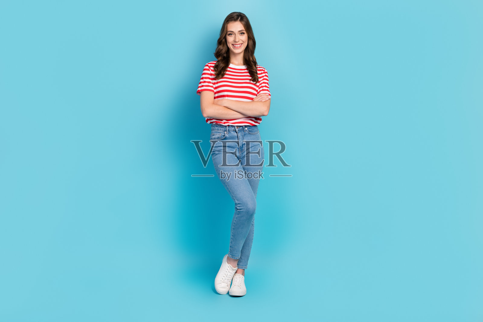 穿着红色T恤的可爱女孩微笑着，双臂交叉，背景为蓝色。照片摄影图片