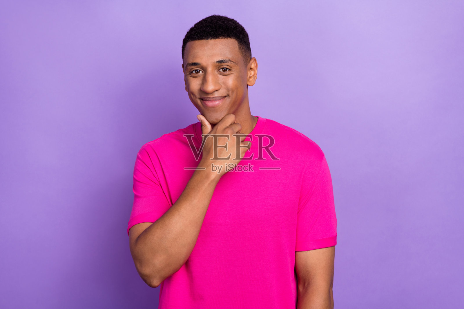 乐观帅气的阳光男士，留着渐变发型，穿着粉色T恤，手肘撑在下巴上，背景为紫色。照片摄影图片