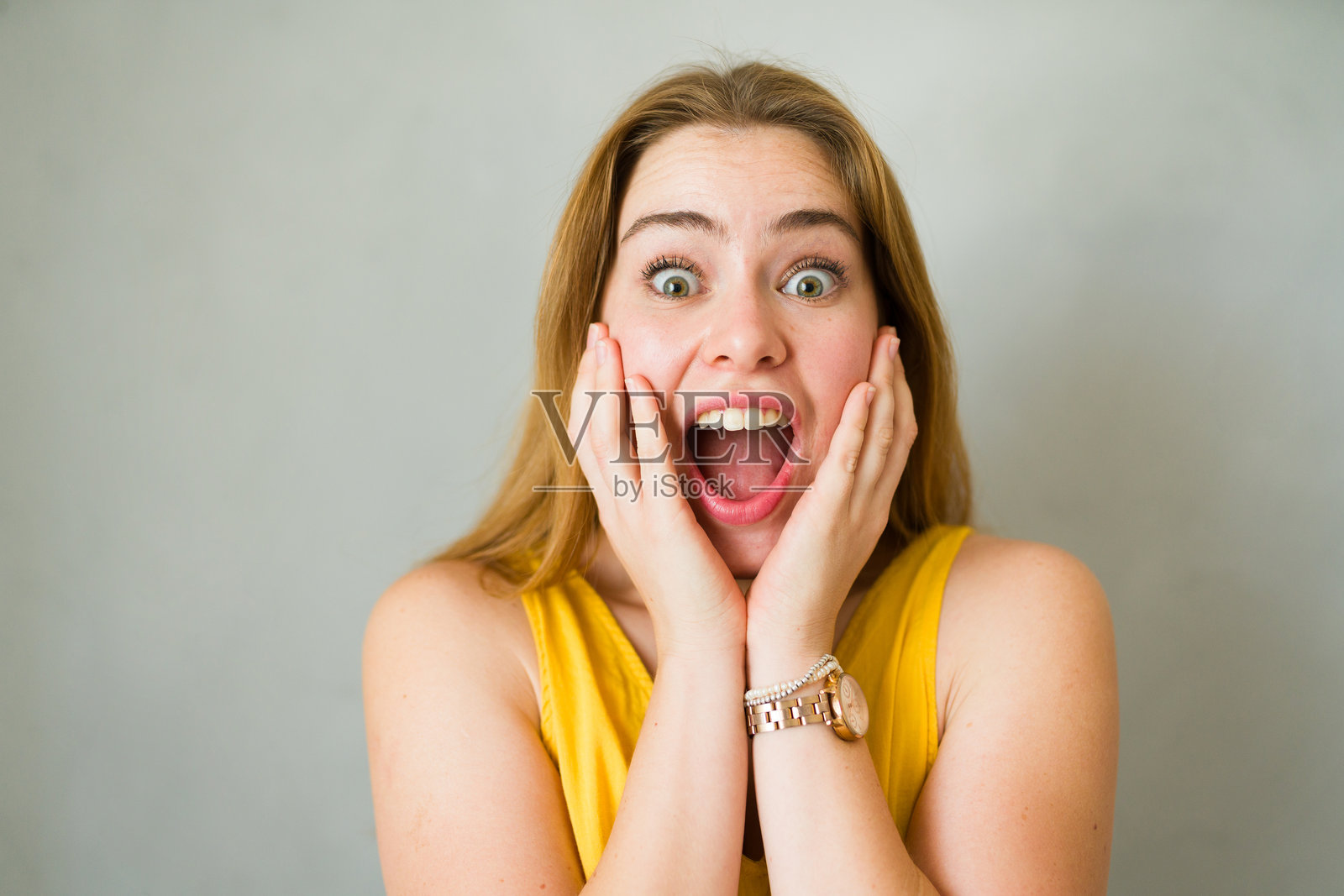 惊讶的年轻女性，金色长发飘逸，双手捧脸，满脸震惊。照片摄影图片