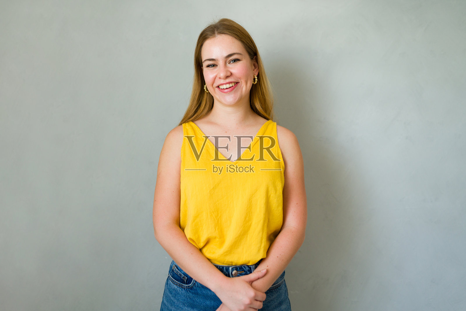 自信的年轻女性在工作室中，穿着黄色衬衫，灿烂微笑。散发着快乐和真实感，适合生活方式概念。照片摄影图片