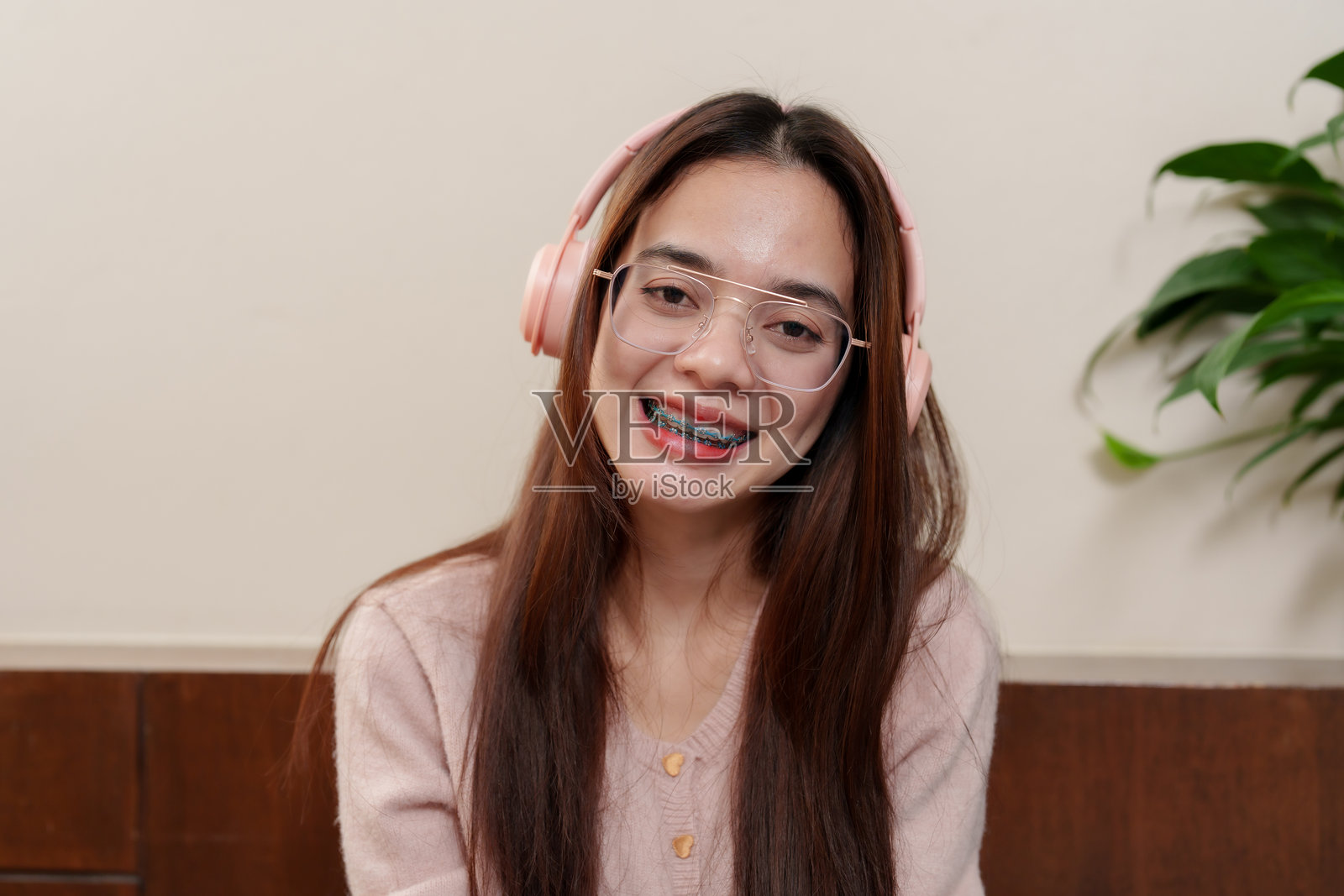 年轻的亚洲女孩，长着棕色的头发，穿着粉色毛衣，戴着眼镜和粉色耳机，面带灿烂的微笑。快乐而清新的表情，强调享受音乐和放松的感觉。照片摄影图片