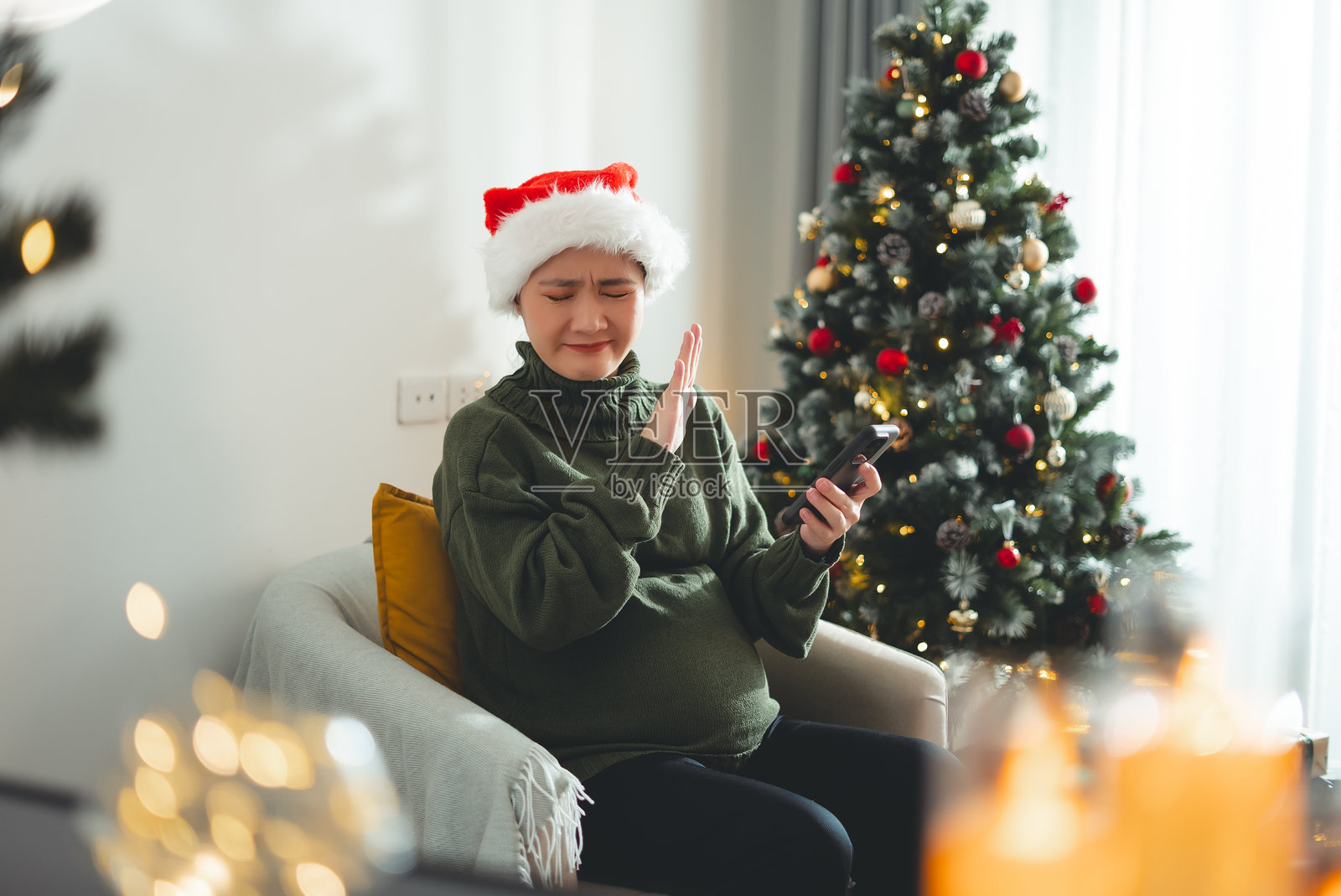 戴着圣诞帽的亚洲孕妇坐在客厅里看着智能手机，感到害怕。照片摄影图片