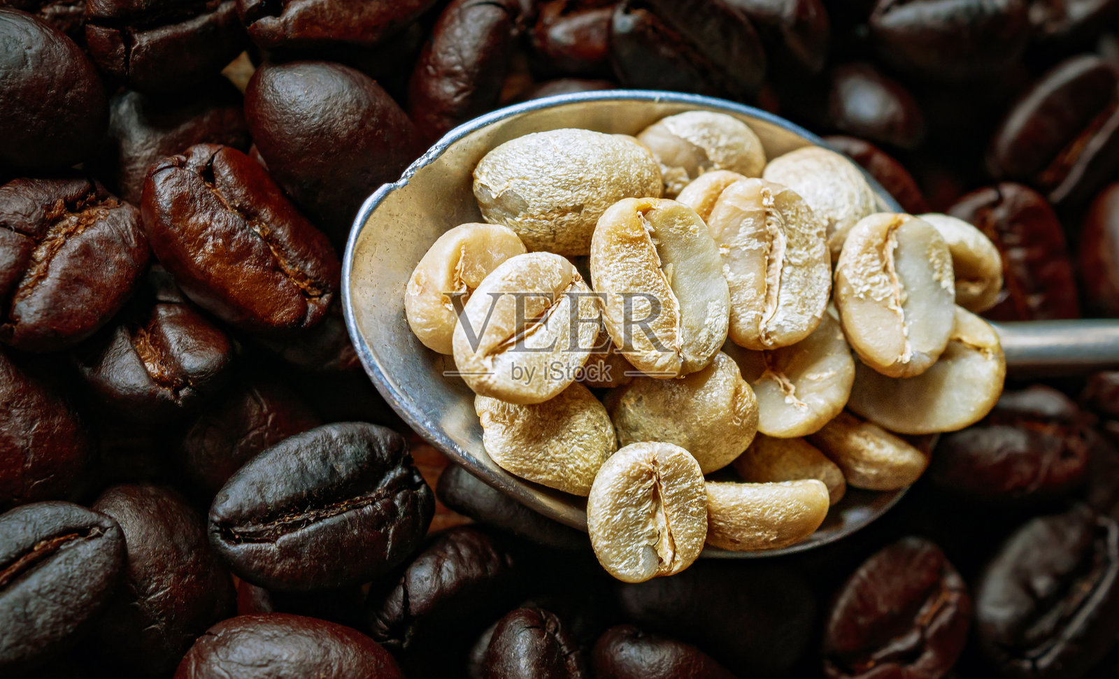 从上方看绿色咖啡豆放在不锈钢勺子上，背景是烘焙咖啡豆，特写，未烘焙咖啡豆的特写。照片摄影图片