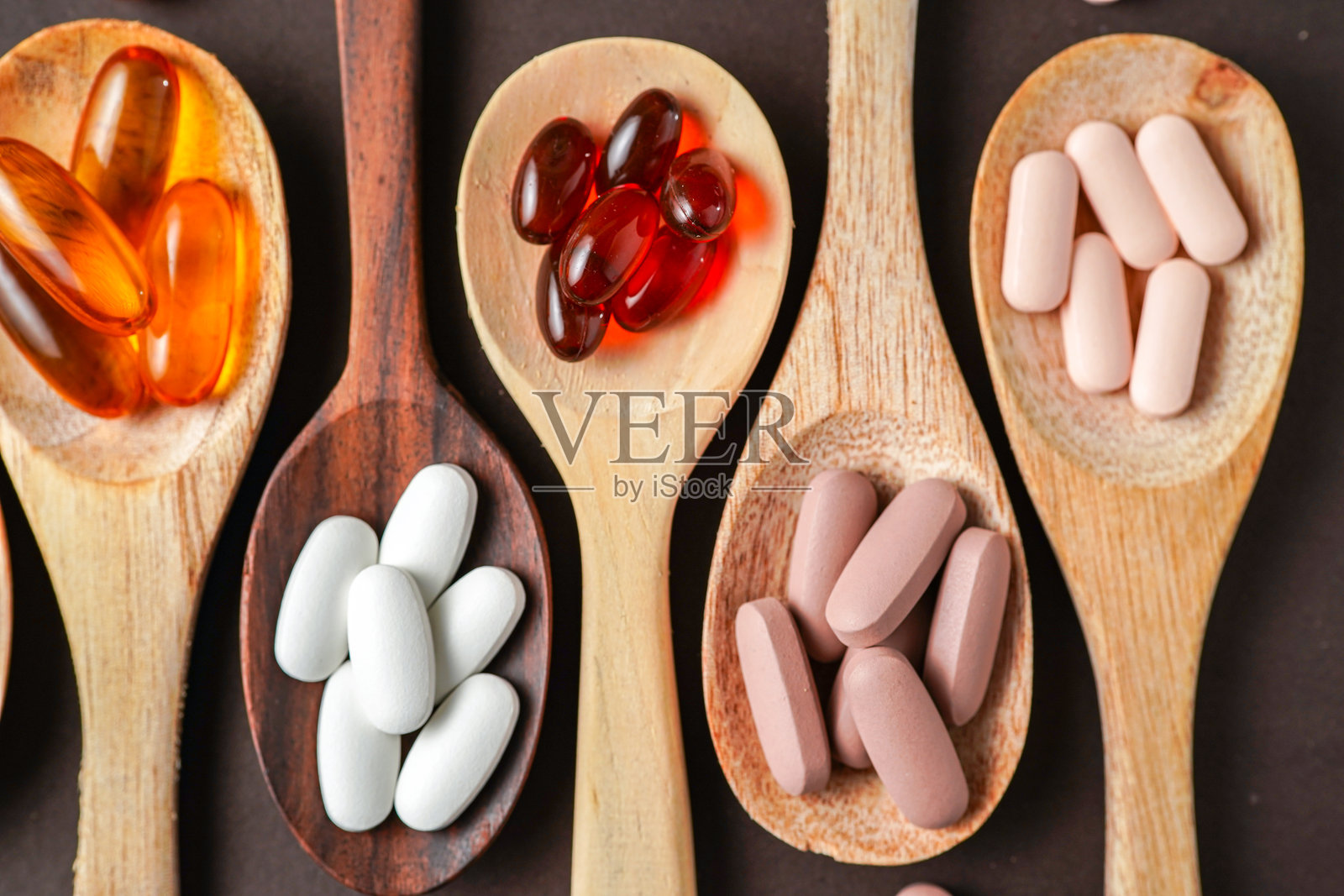 木勺中的维生素草本胶囊、鱼油和食品补充剂，背景为深色。照片摄影图片