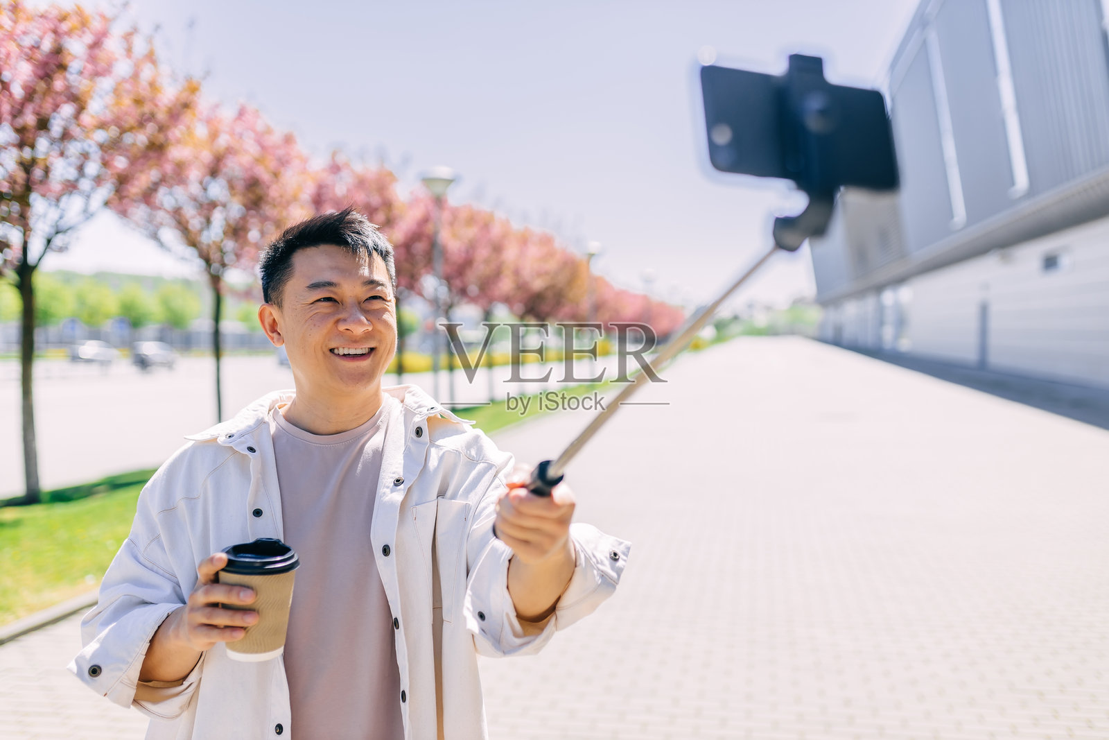 年轻的亚洲男孩用自拍杆拿着手机与人通话，展示城市风景。照片摄影图片