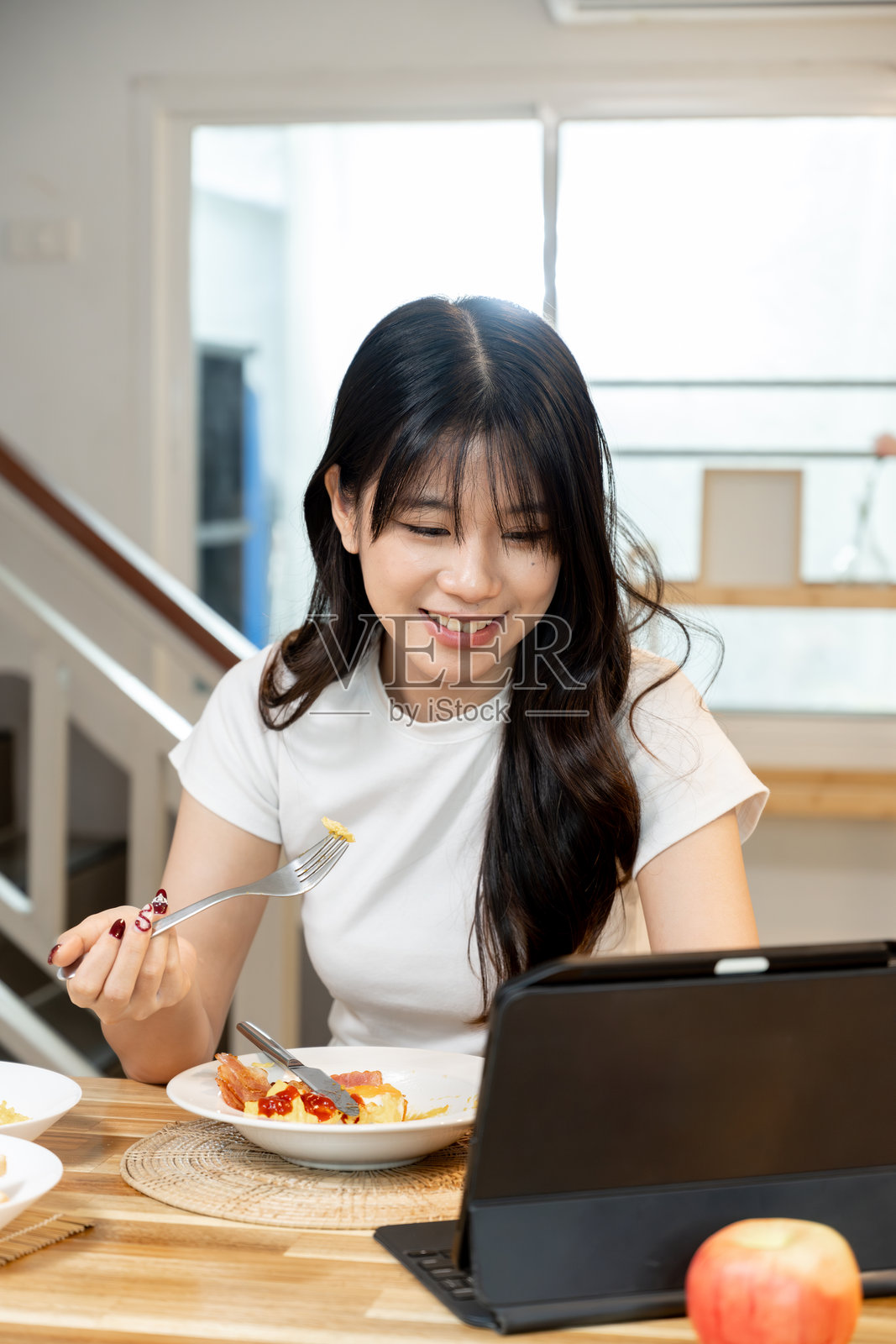 年轻的亚洲女性在吃早餐，同时通过平板电脑参加在线会议照片摄影图片