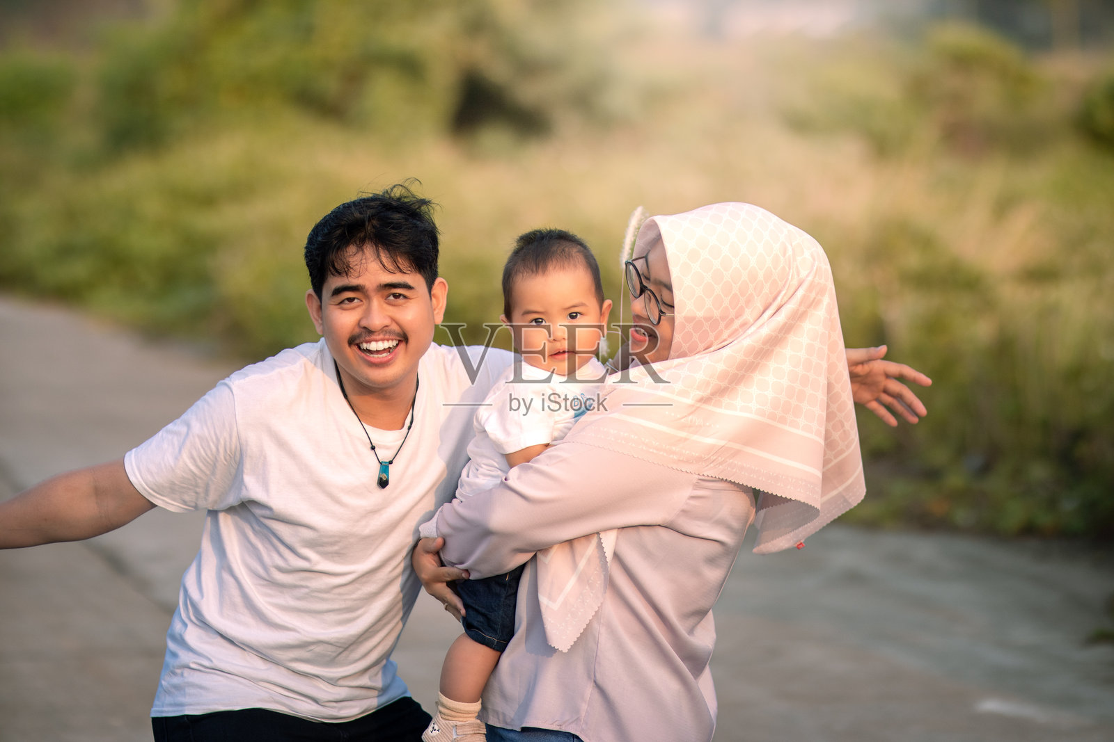 一家看起来快乐的家庭，母亲、父亲和婴儿男孩都在微笑，父亲大声笑着，母亲抱着婴儿男孩。照片的氛围在大自然中。照片摄影图片