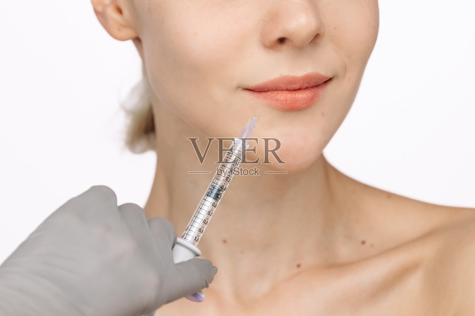 一位年轻美丽的女性在白色摄影棚背景下接受美容注射。特写镜头突显了美容医学和注射在保持青春与光彩中的重要性。照片摄影图片