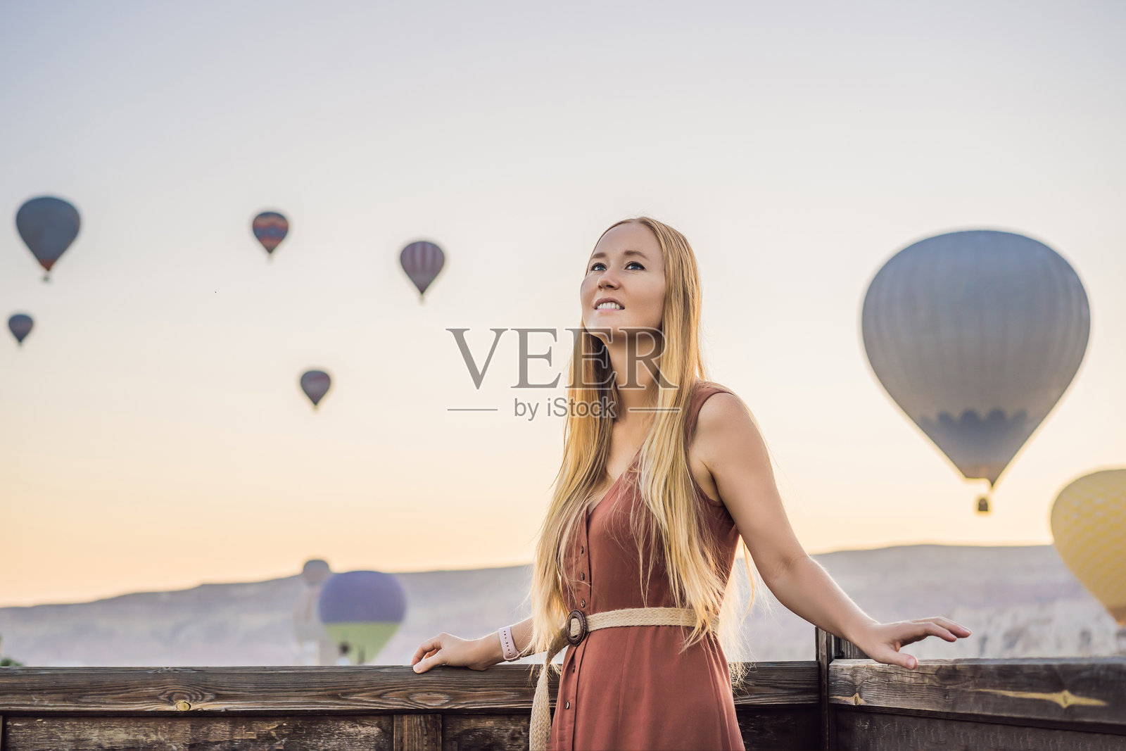 在土耳其卡帕多奇亚，一位女游客欣赏热气球。快乐的土耳其旅行概念。女子在山顶享受美妙的景色。照片摄影图片