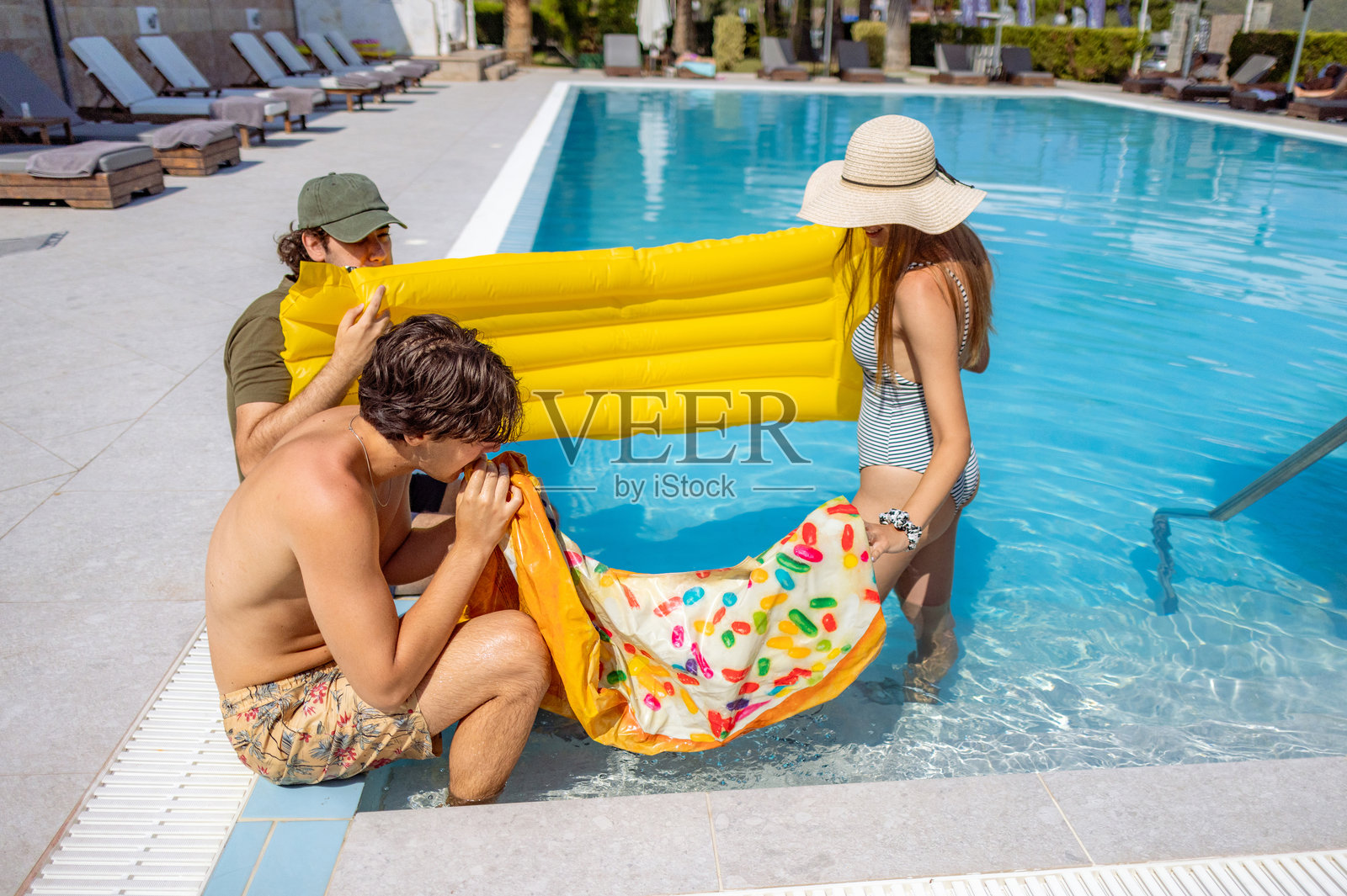 在泳池旁与朋友们一起给充气床垫充气照片摄影图片