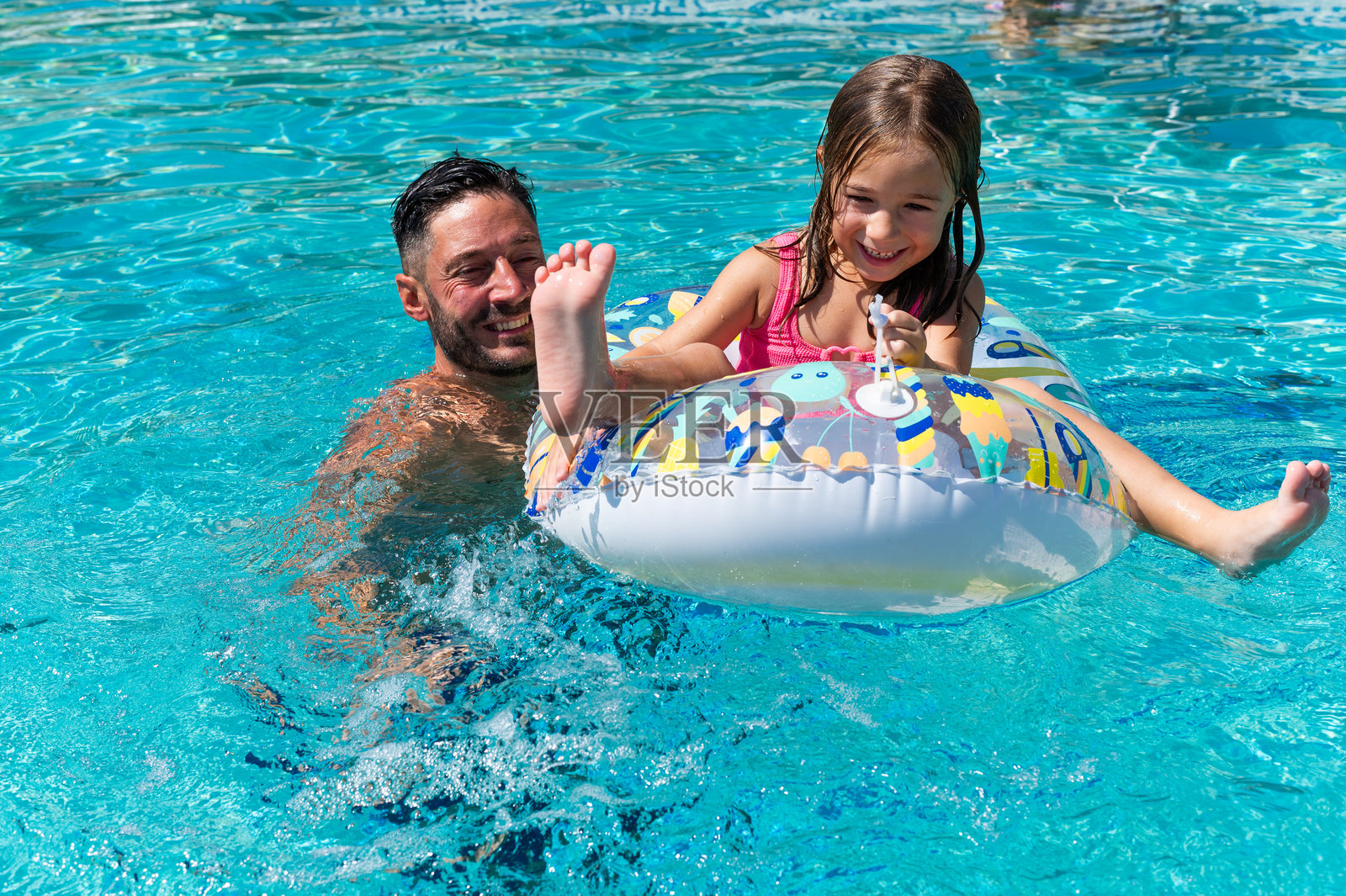 爸爸在游泳池里推着女儿坐在充气圈上照片摄影图片