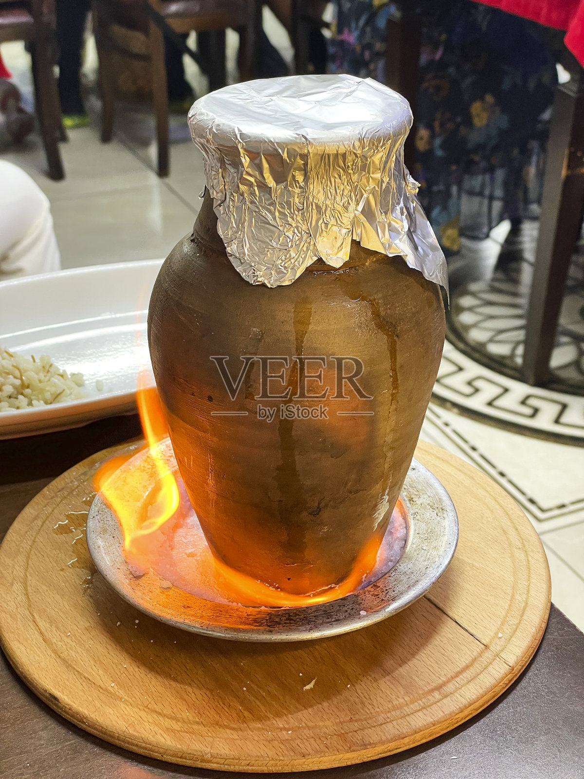 在温馨的餐厅环境中，传统陶器用铝箔封住，旁边是一道燃烧的菜肴，土耳其烤肉在陶罐中烹饪。照片摄影图片