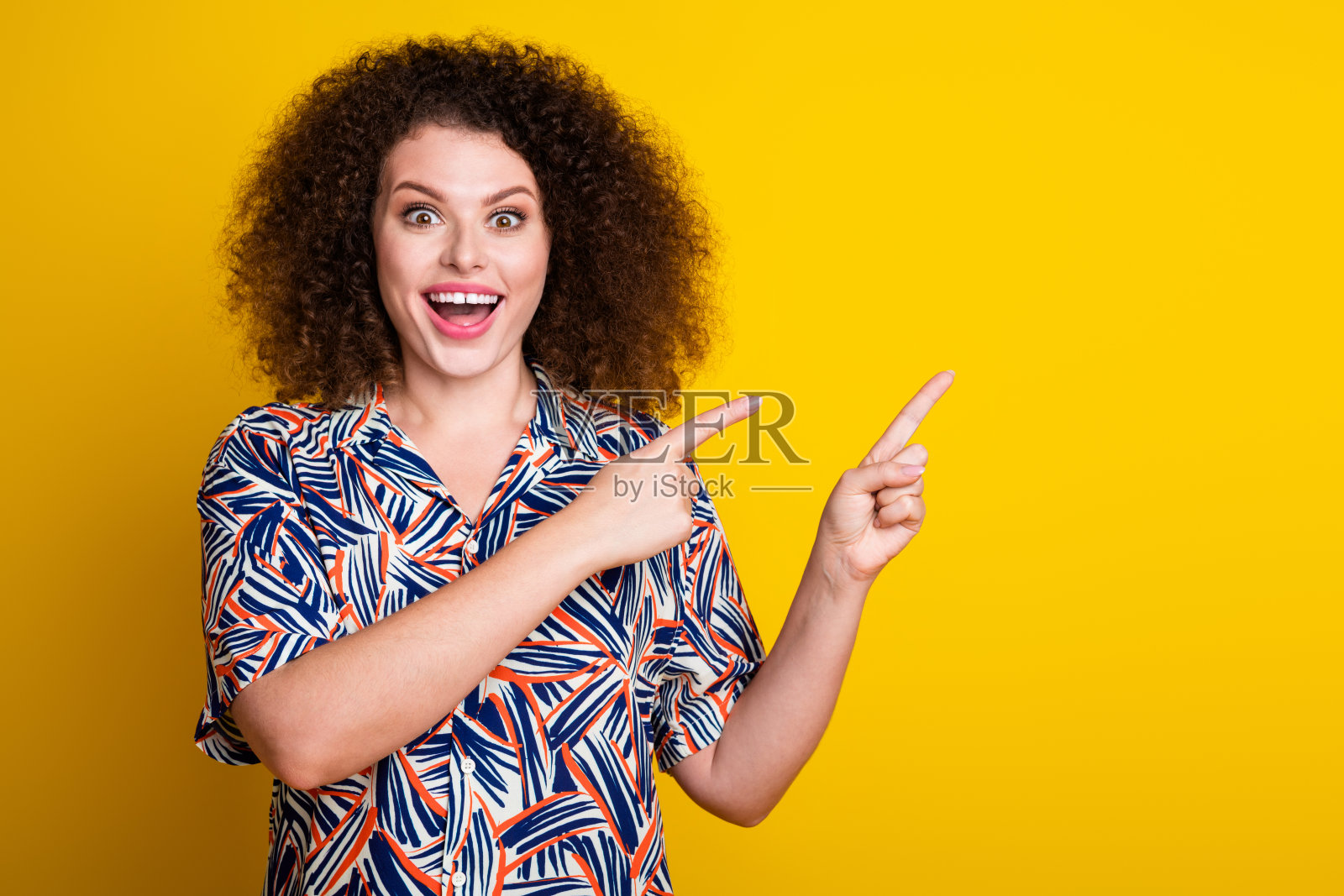 漂亮年轻女孩的照片肖像，指向空白处，穿着时尚多彩的服装，背景为黄色。照片摄影图片
