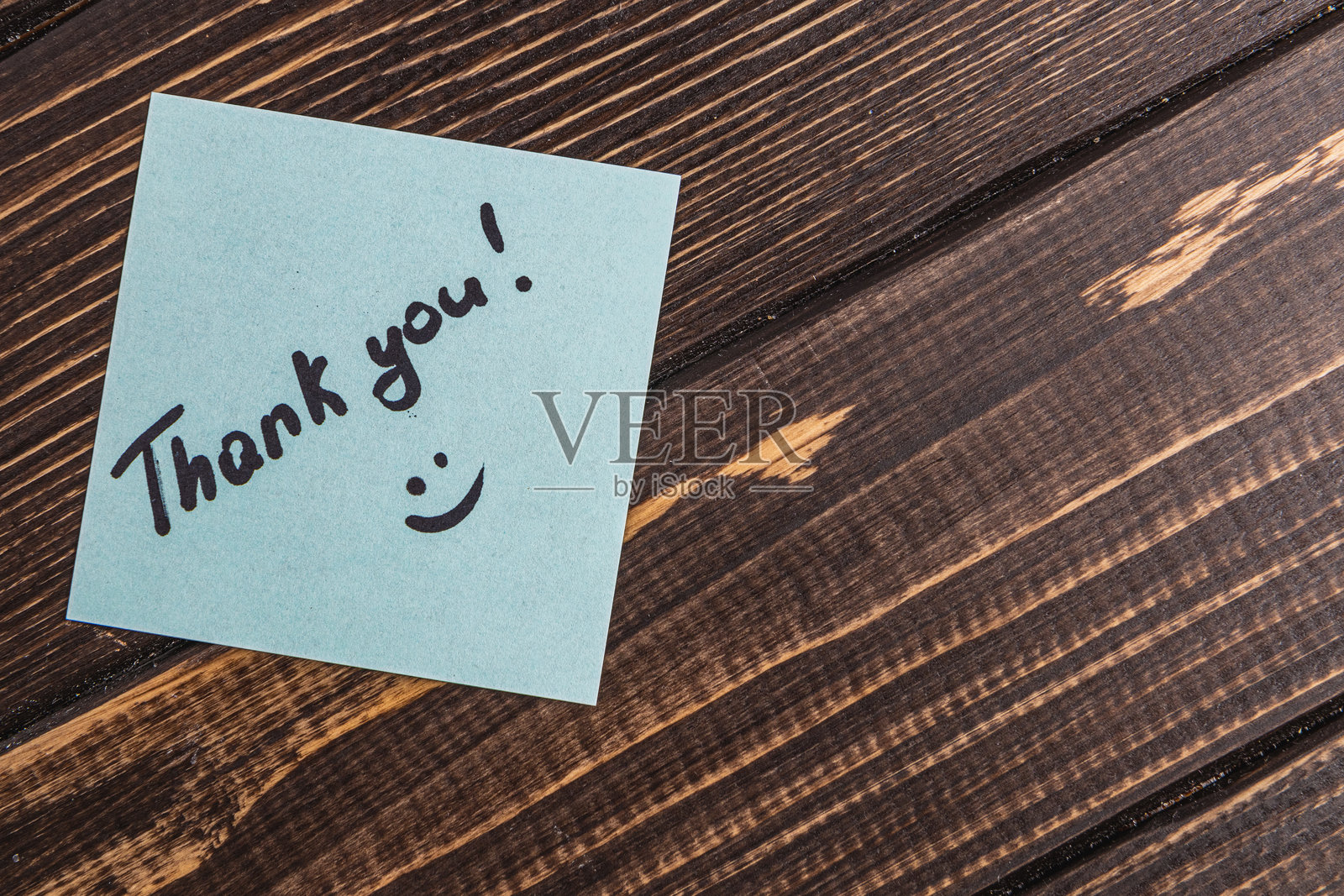 在木桌上，浅绿色纸上写着“谢谢”一词和一个表情符号照片摄影图片