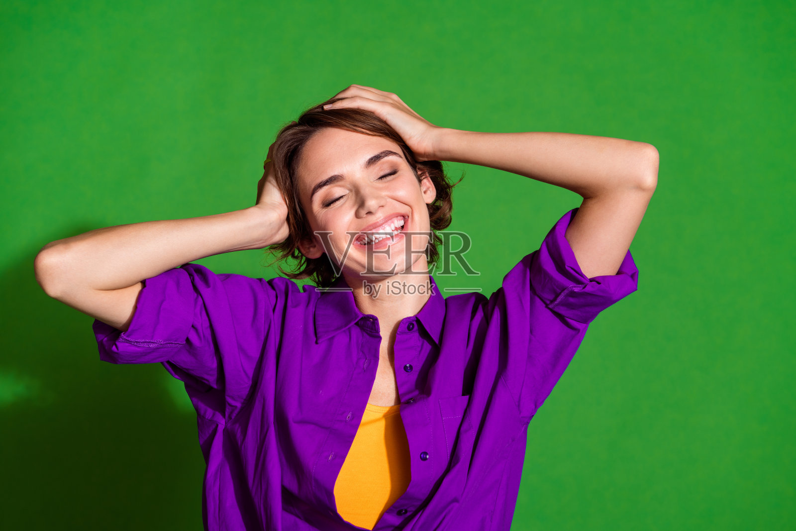 年轻迷人的女孩肖像照片，棕色头发，触摸头部，幸福的一天，穿着紫色衬衫，背景为绿色。照片摄影图片