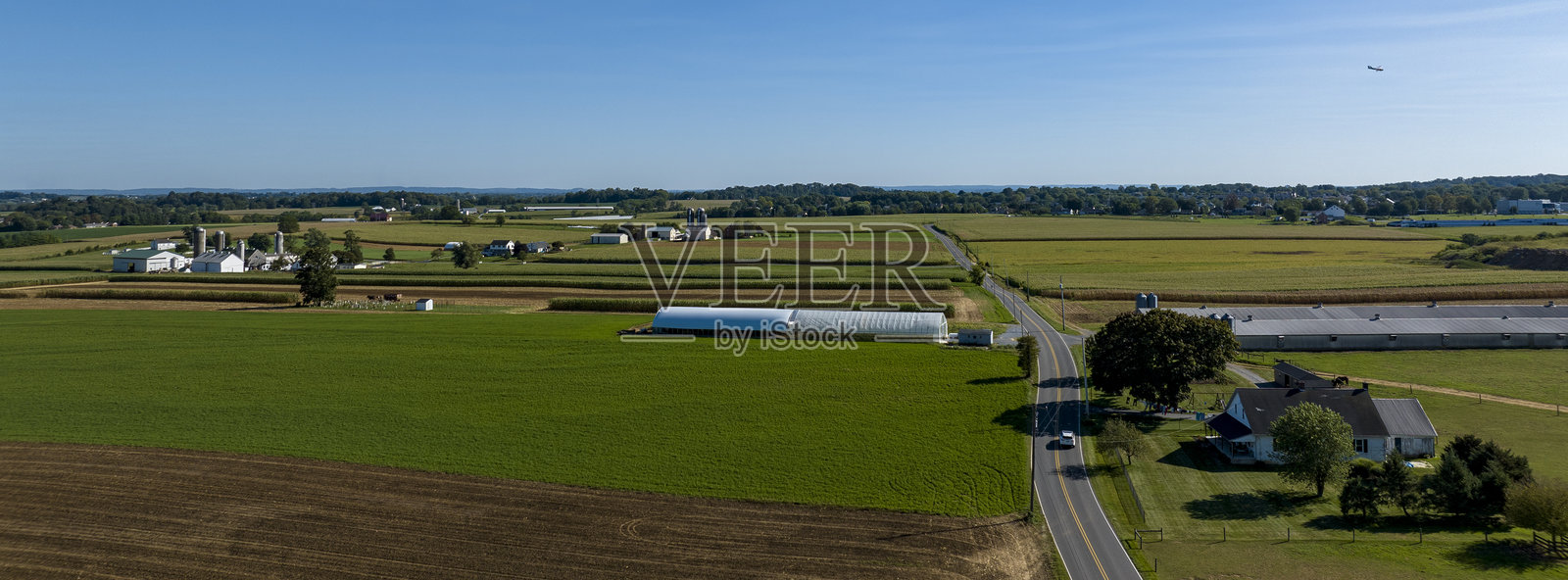 清澈天空下的乡村风景鸟瞰图，展现了田野、农场和蜿蜒的道路。照片摄影图片