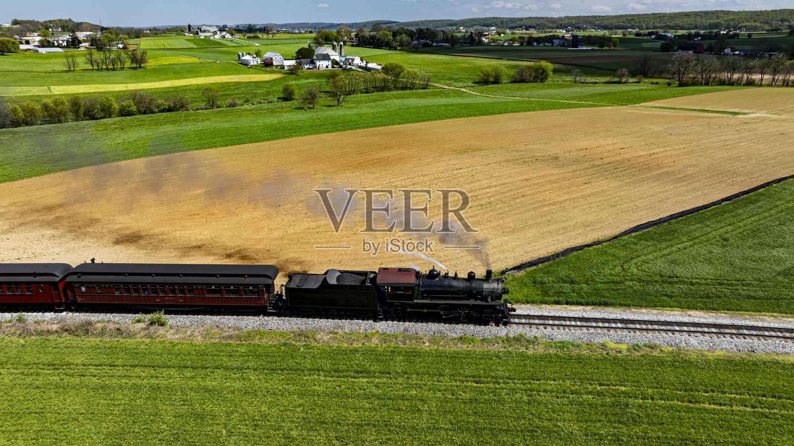 蒸汽机车在阳光明媚的白天穿越郁郁葱葱的乡村农田照片摄影图片