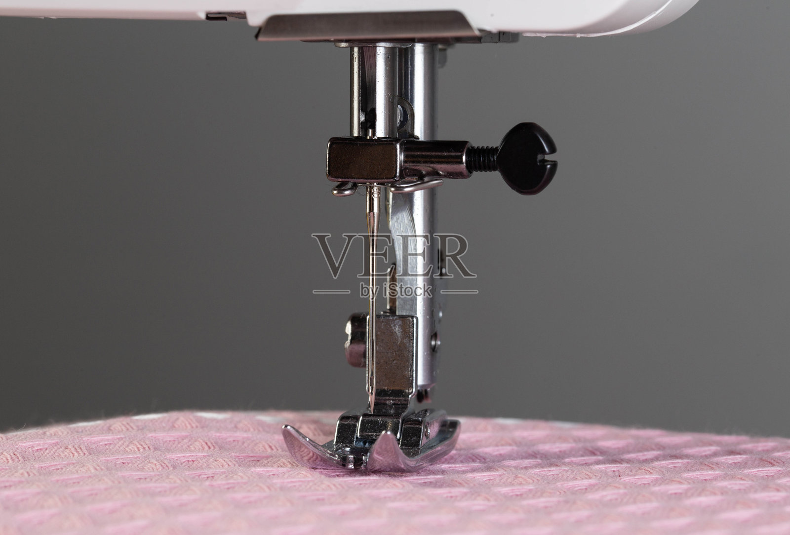 一根带针夹的针和缝纫机脚，背景是粉色布料。特写，工业。文本留白。裁缝服务。照片摄影图片