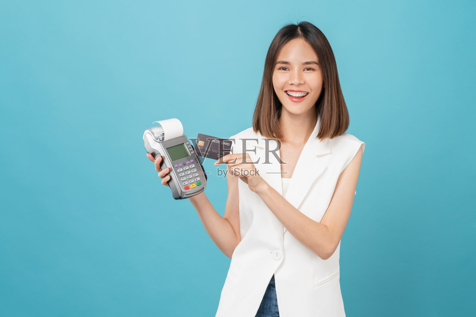 快乐美丽的亚洲女性手持信用卡在读卡机上进行支付，背景为蓝色。照片摄影图片