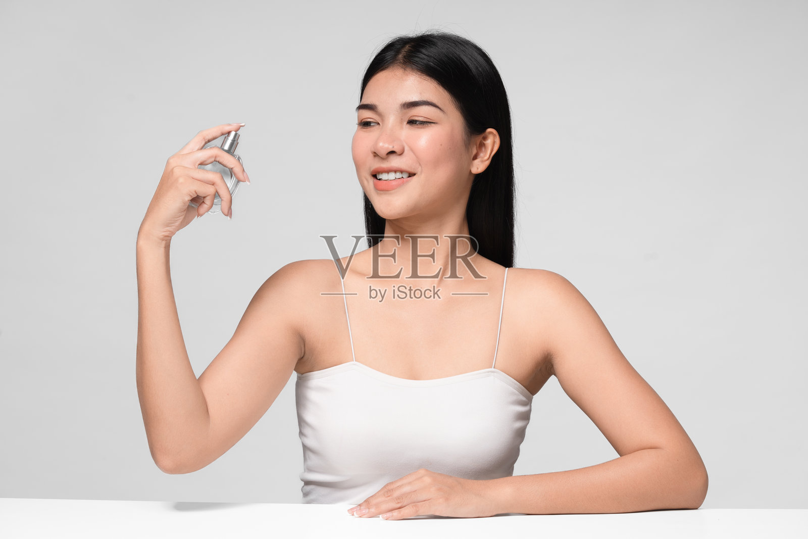 手持香水的女性。完美妆容的女性照片，背景为灰色。美容概念。照片摄影图片