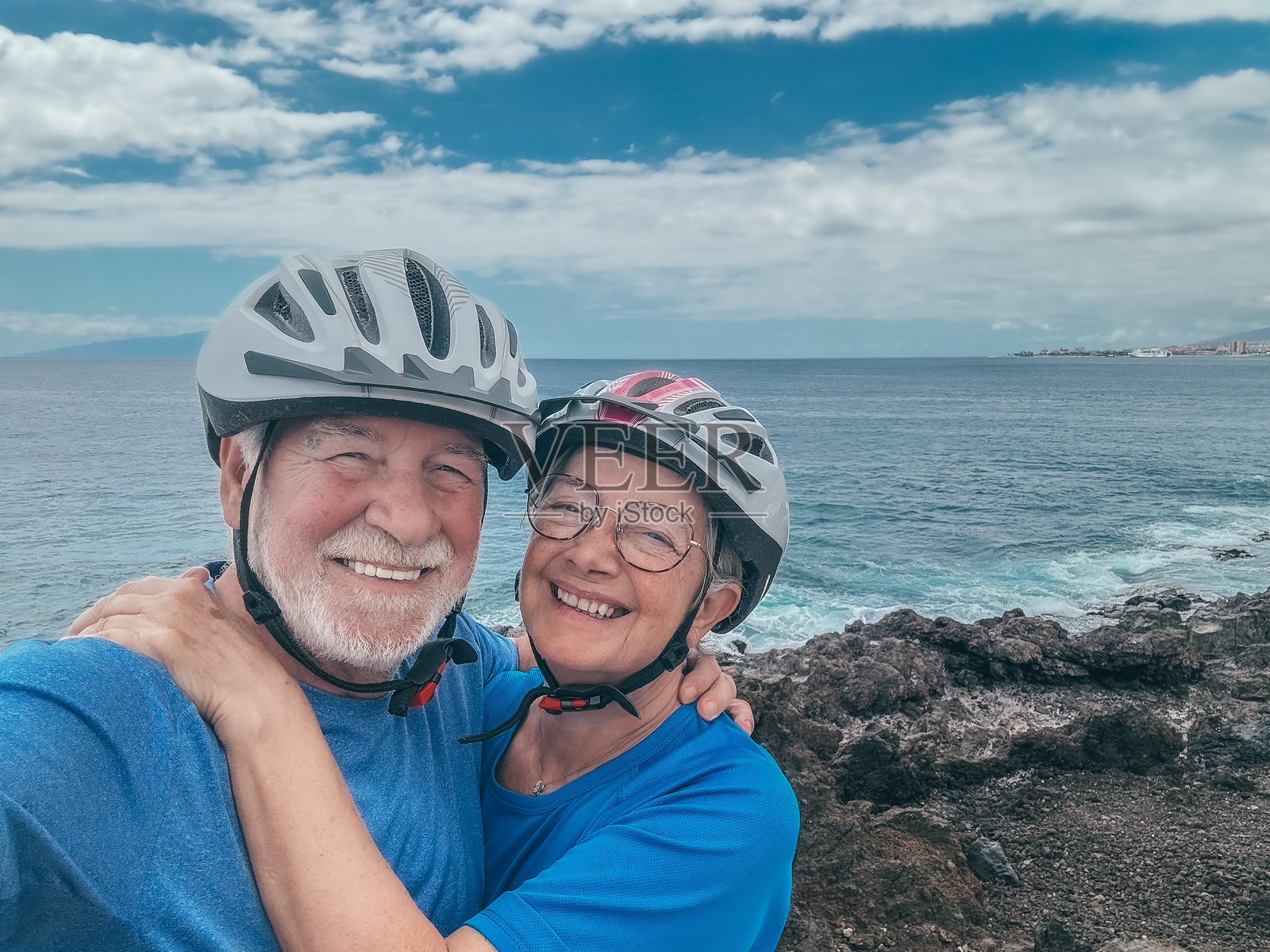 快乐的老年夫妇骑着电动自行车在海边拍照，拥抱着看向镜头，享受退休后的健康生活。水面上的地平线。照片摄影图片