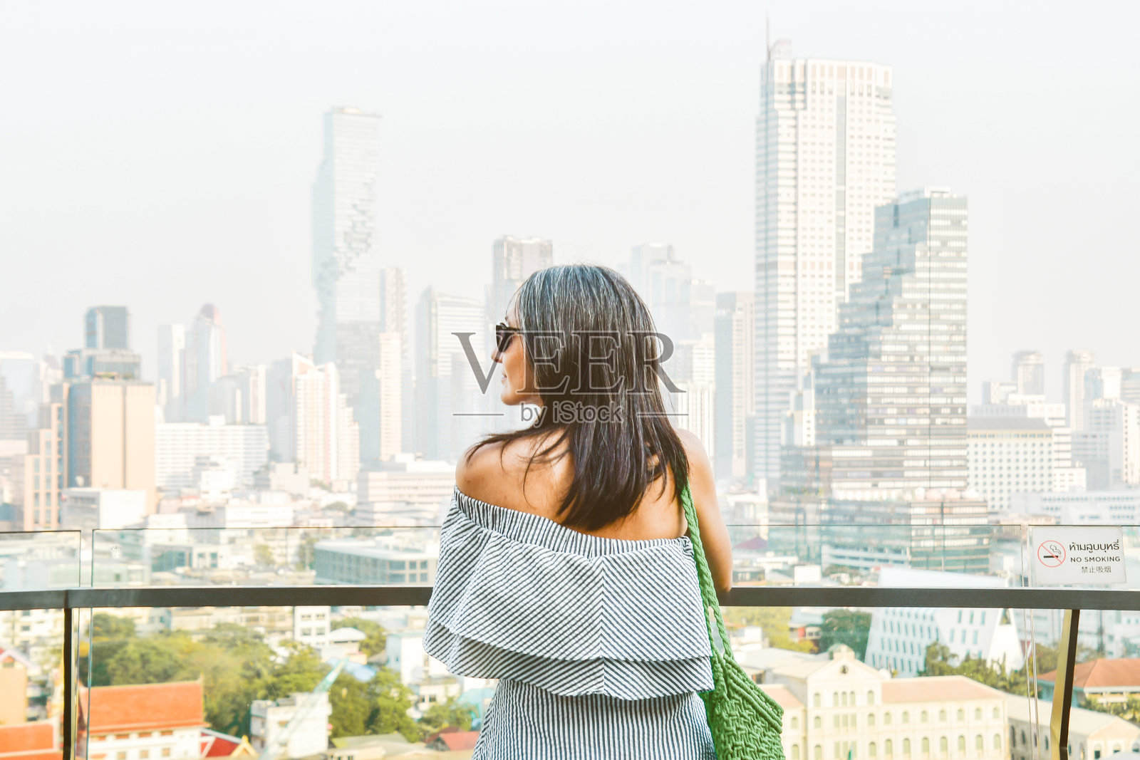 年轻漂亮的女性游客肖像，享受曼谷城市天际线全景。著名地标购物中心位于城市观景台。侧面视图特写，明亮滤镜。照片摄影图片