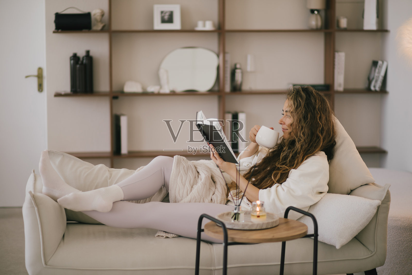 年轻女性坐在舒适的客厅沙发上，阅读书籍并喝茶。照片摄影图片