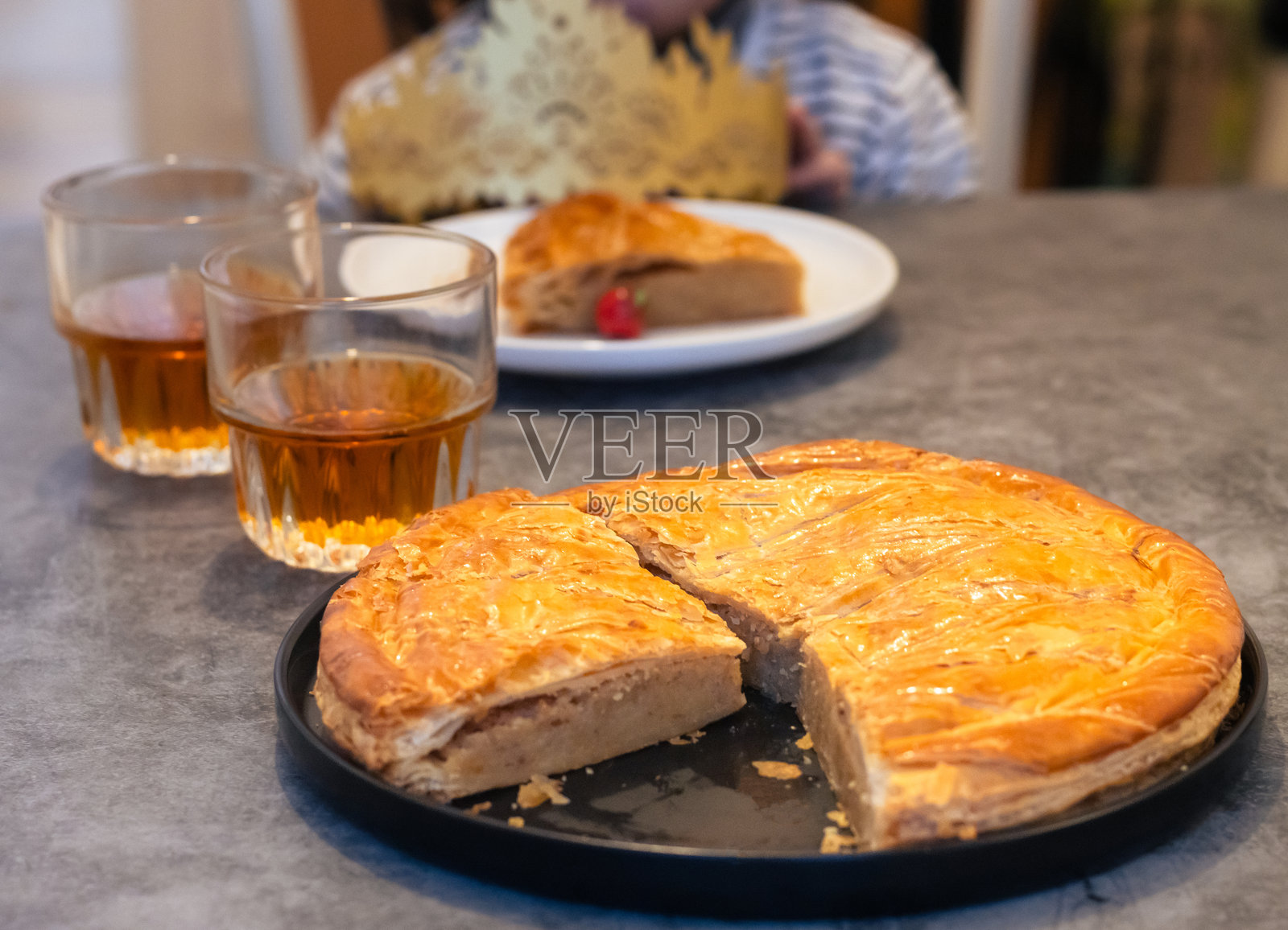 一盘切好的传统法式国王饼（galette des rois），旁边有几杯苹果酒。照片摄影图片