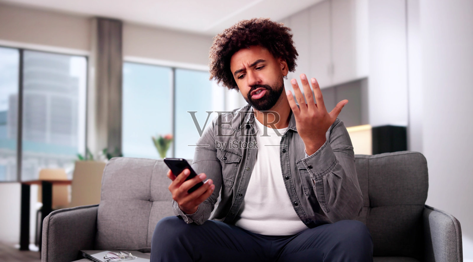 担忧的年轻男子坐在沙发前看着智能手机照片摄影图片