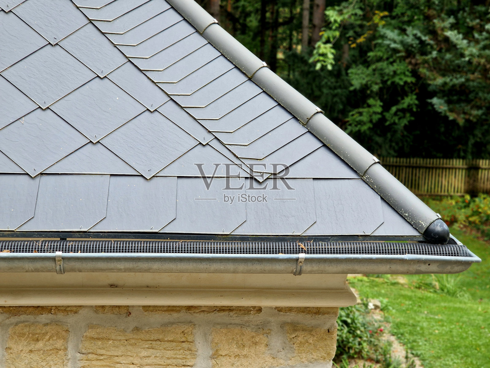 设计良好的塑料网覆盖在排水沟内部，树叶不会掉入其中。堵塞的排水管已成为过去。烧制的屋顶瓦。照片摄影图片