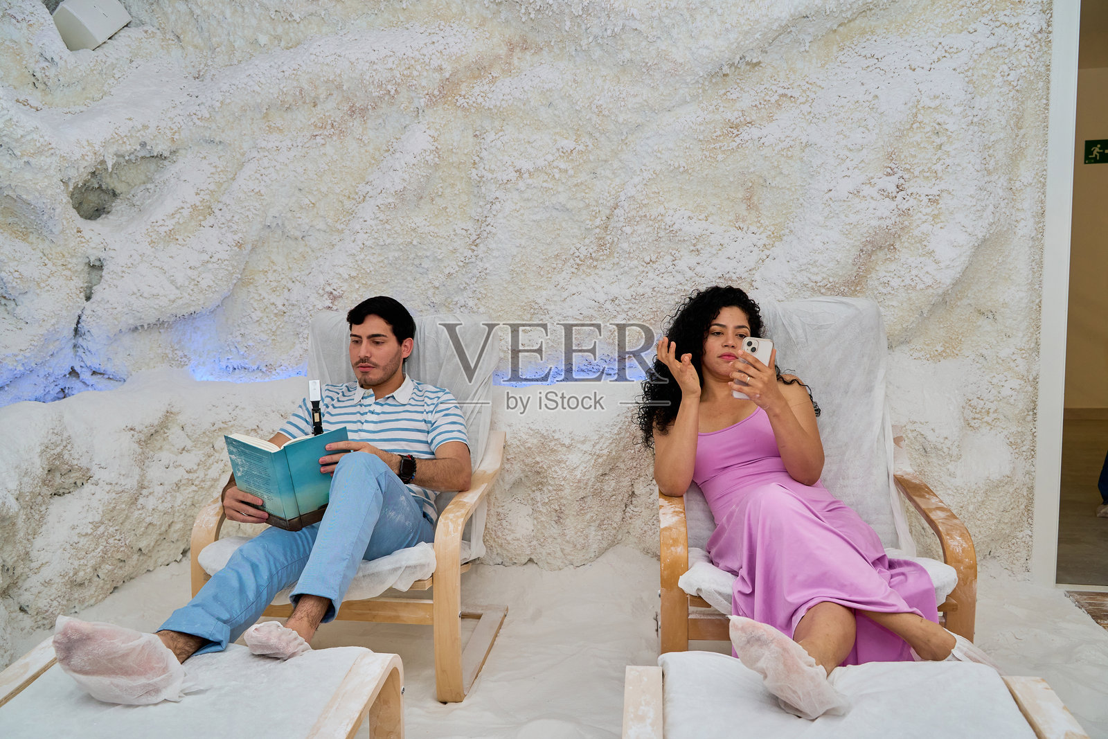 男子在盐洞疗法中阅读书籍，女子使用智能手机。照片摄影图片