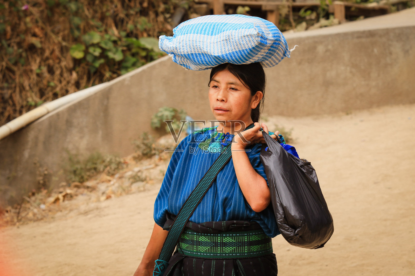 危地马拉妇女在乡村小路上走着，头上顶着一个篮子。照片摄影图片