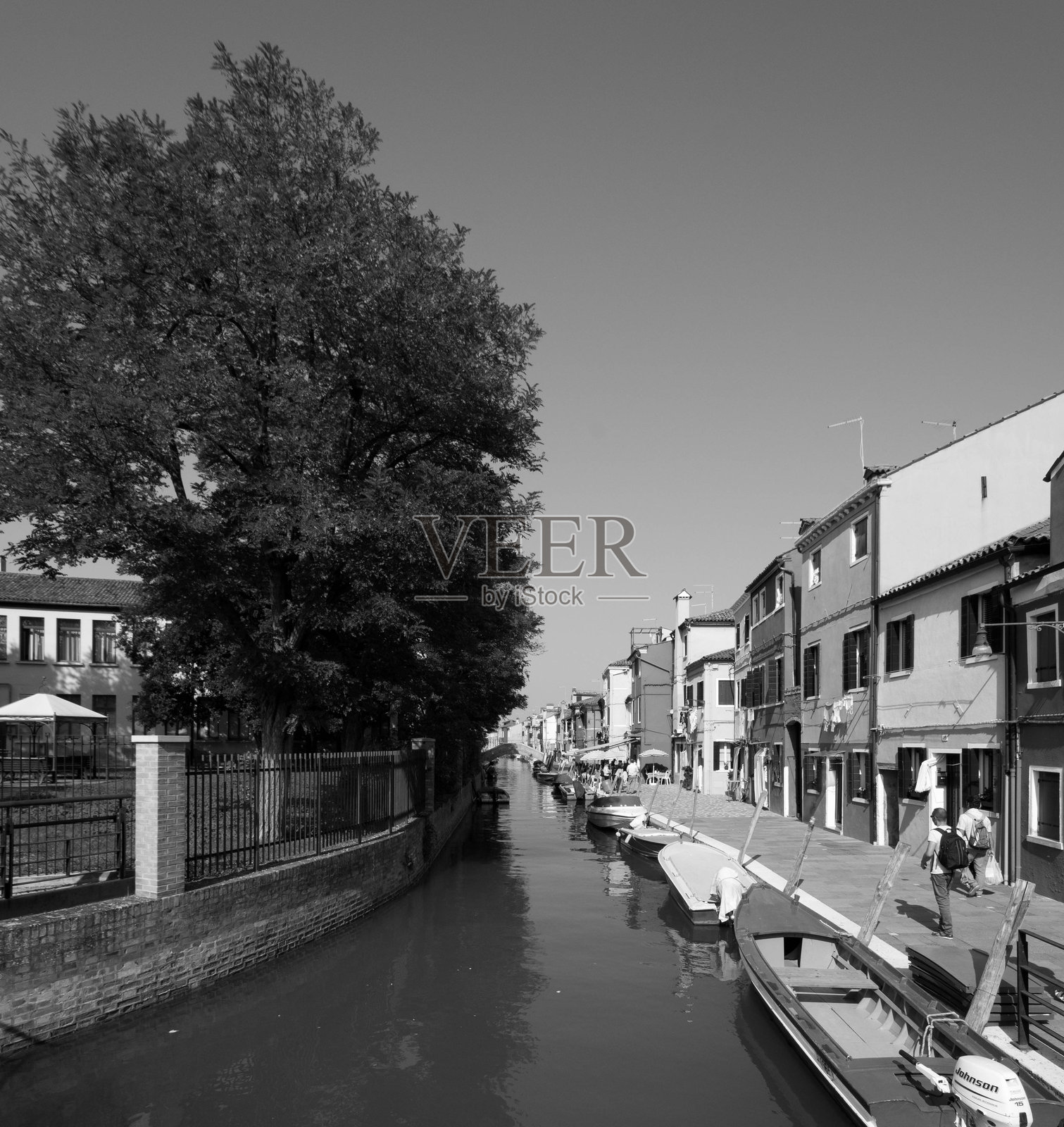 威尼斯的运河，停泊着小船，人们在阳光明媚的夏日里漫步，黑白色调。照片摄影图片