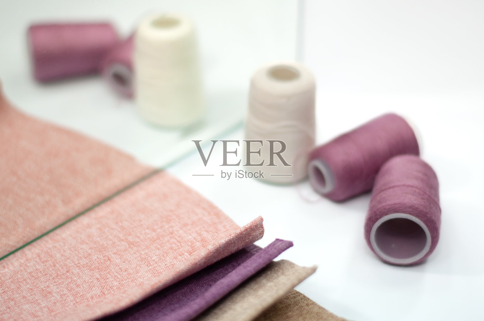 粉色、紫色和米色的布料样本，紫色缝纫线。照片摄影图片