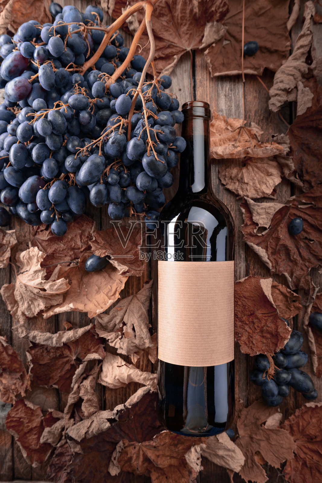 一瓶红酒、蓝色葡萄和干枯的藤叶。照片摄影图片