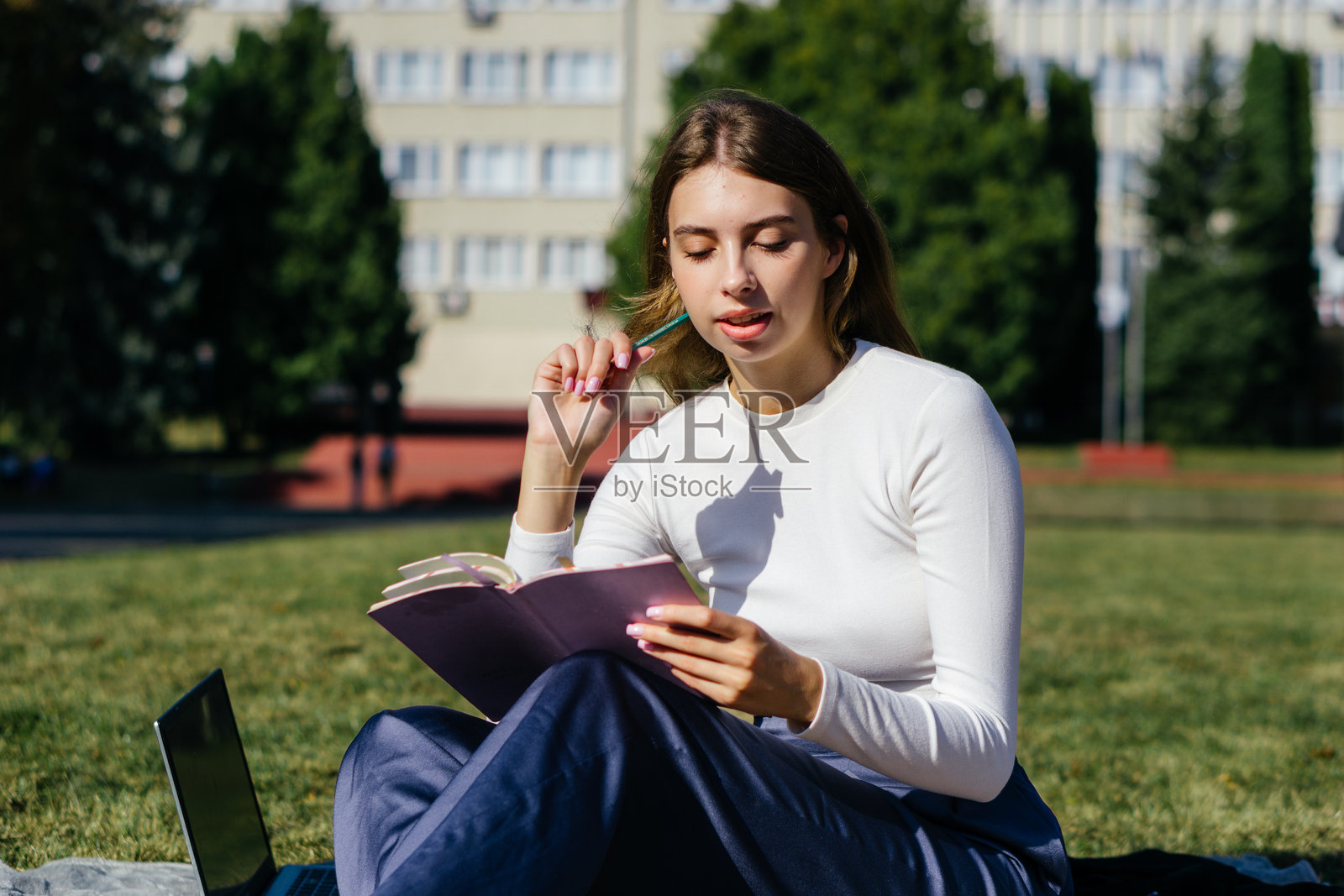 大学校园的女学生在夏季假期的绿草地上使用笔记本电脑学习并做笔记。照片摄影图片
