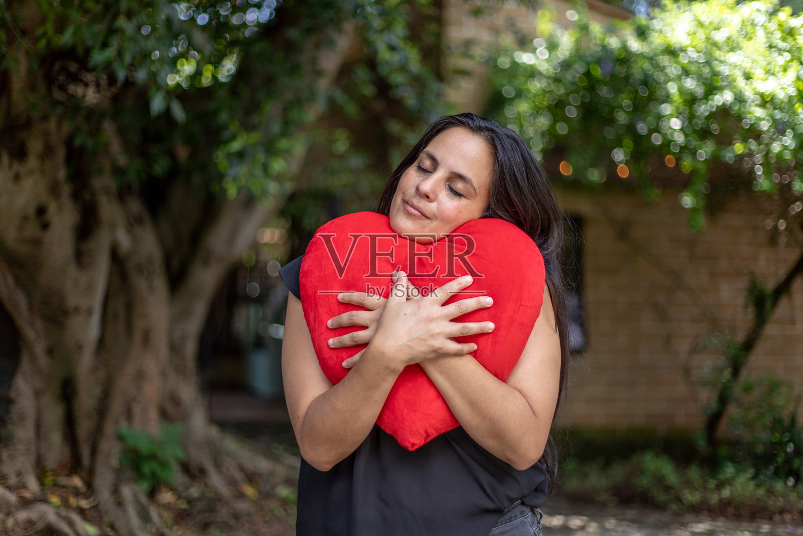 一位西班牙裔女性亲切地拥抱着一个红色的心形抱枕 - 爱或心脏健康概念照片摄影图片