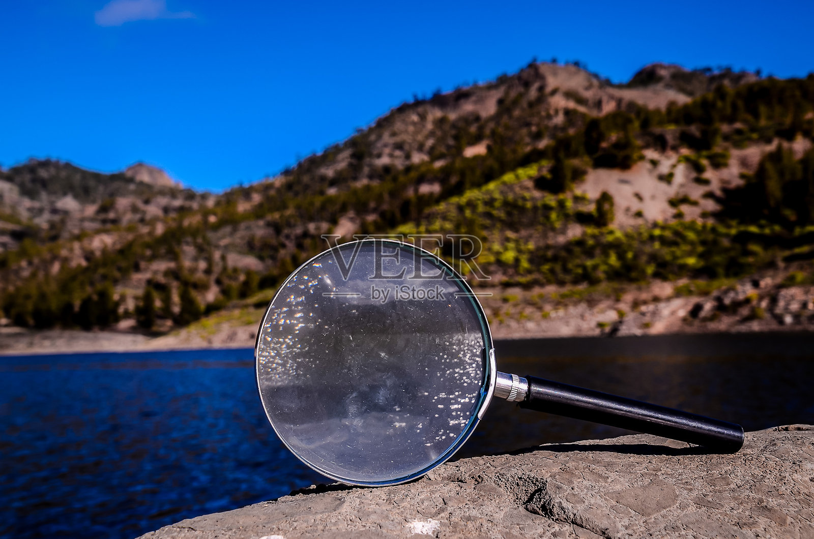 一只放大镜放在水边的一块石头上照片摄影图片
