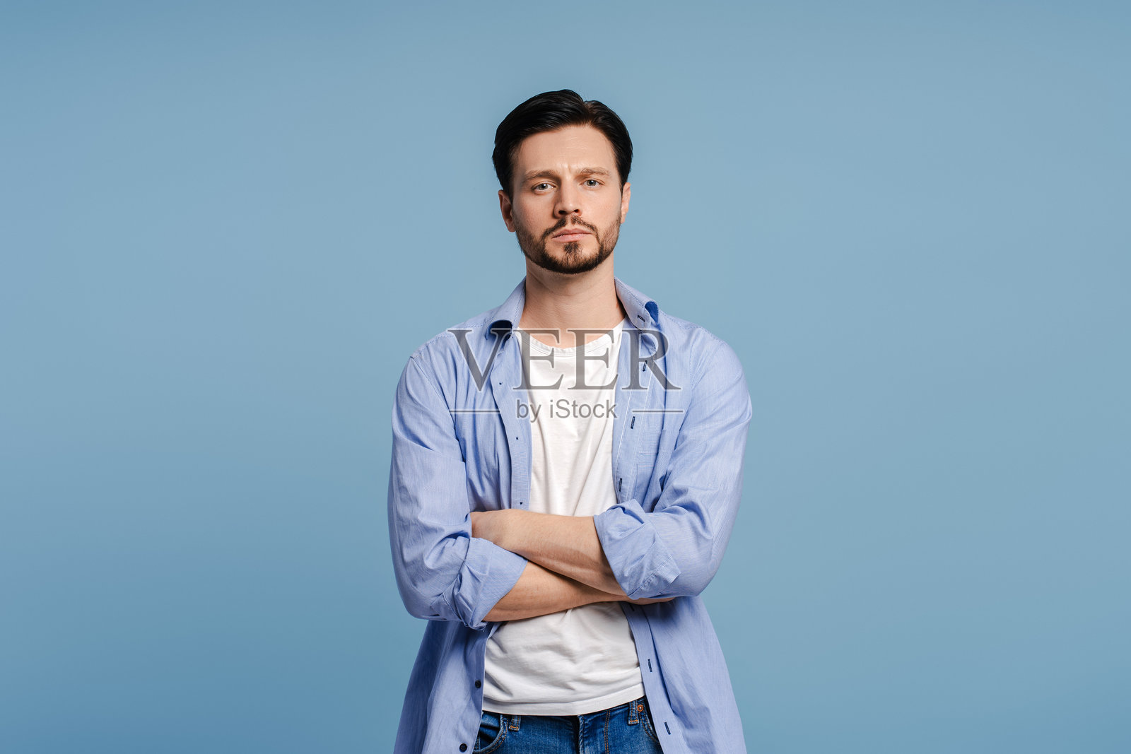 神情严肃的男子交叉双臂，在蓝色背景下注视镜头照片摄影图片