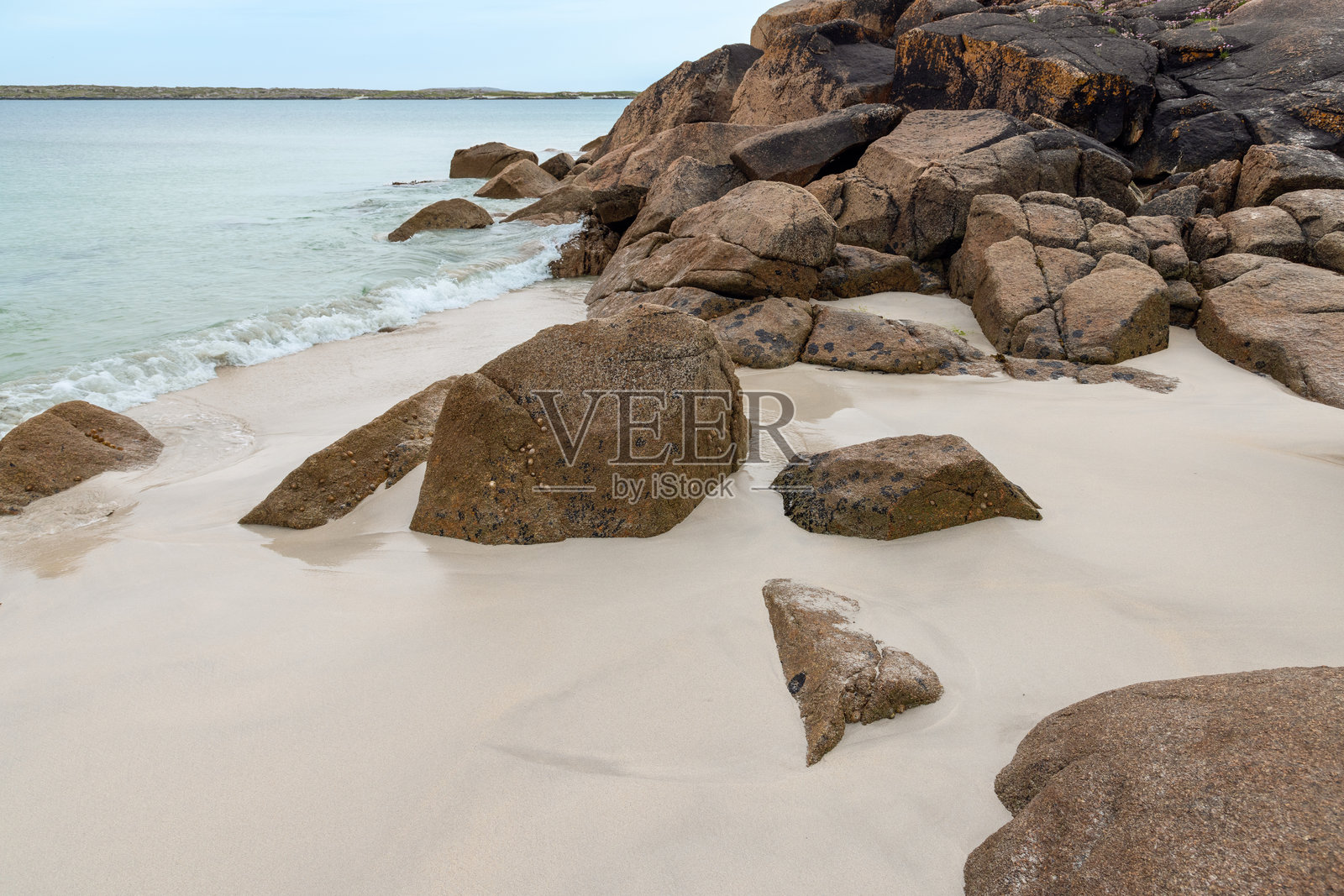 爱尔兰古尔廷湾的岩石海岸，巨石散落在柔软的沙滩上。大西洋清澈而浅的海水轻轻拍打着海岸线。照片摄影图片