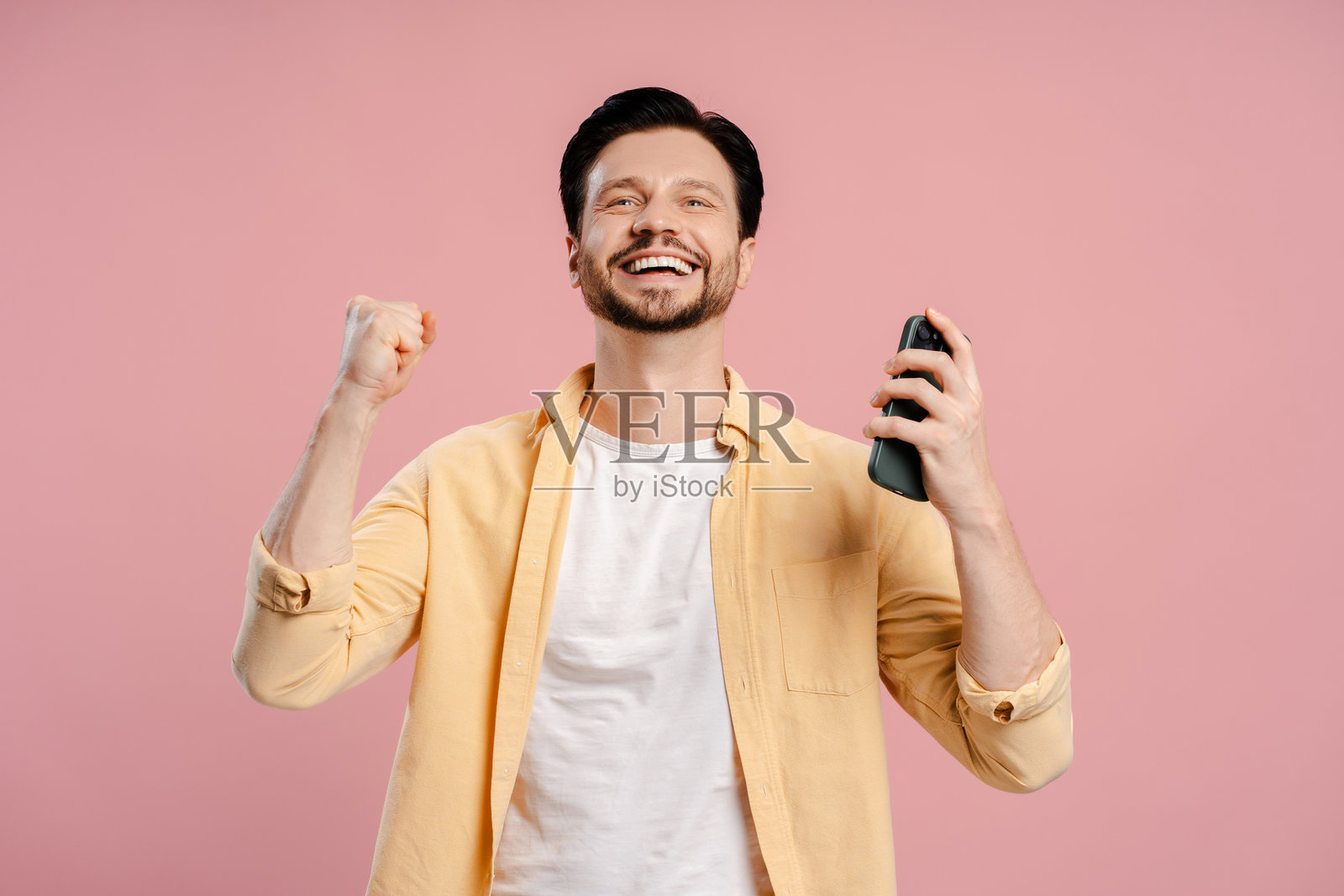 兴奋的男人在粉红色背景上用智能手机庆祝成功照片摄影图片