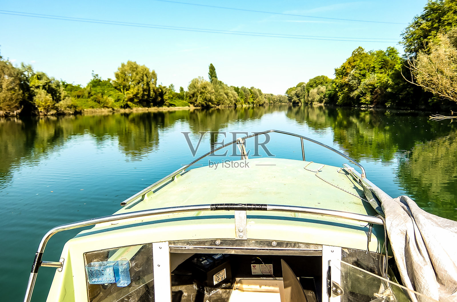 一艘船正沿着河流行驶，船头有一个绿色的遮篷。照片摄影图片