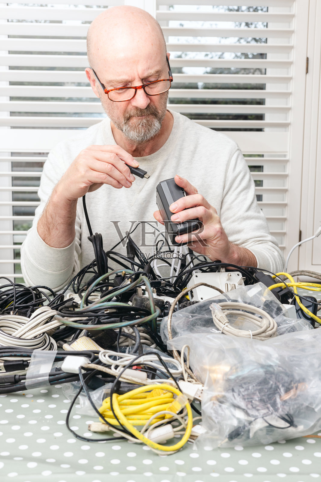 困惑的老年男子在一堆混乱的电线和电缆中寻找正确的充电设备连接线照片摄影图片