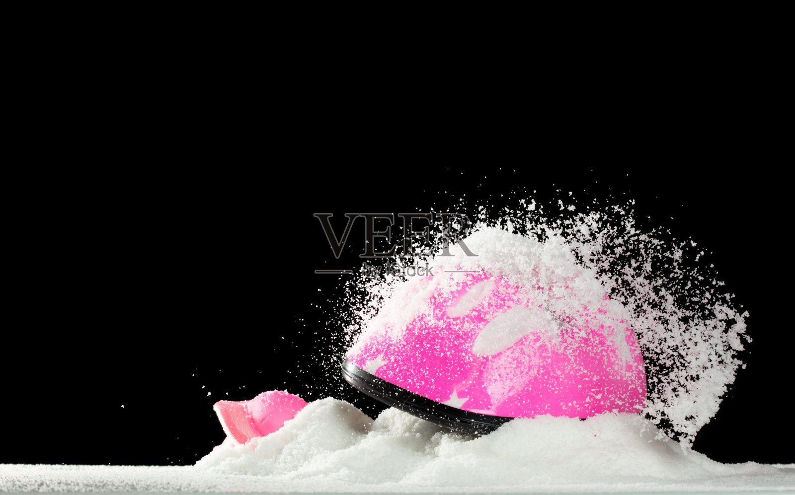 粉色安全头盔在冬季被雪覆盖。冬季的雪使自行车道路变得滑腻，因此安全头盔可以保护儿童免受危险。黑色背景隔离。照片摄影图片