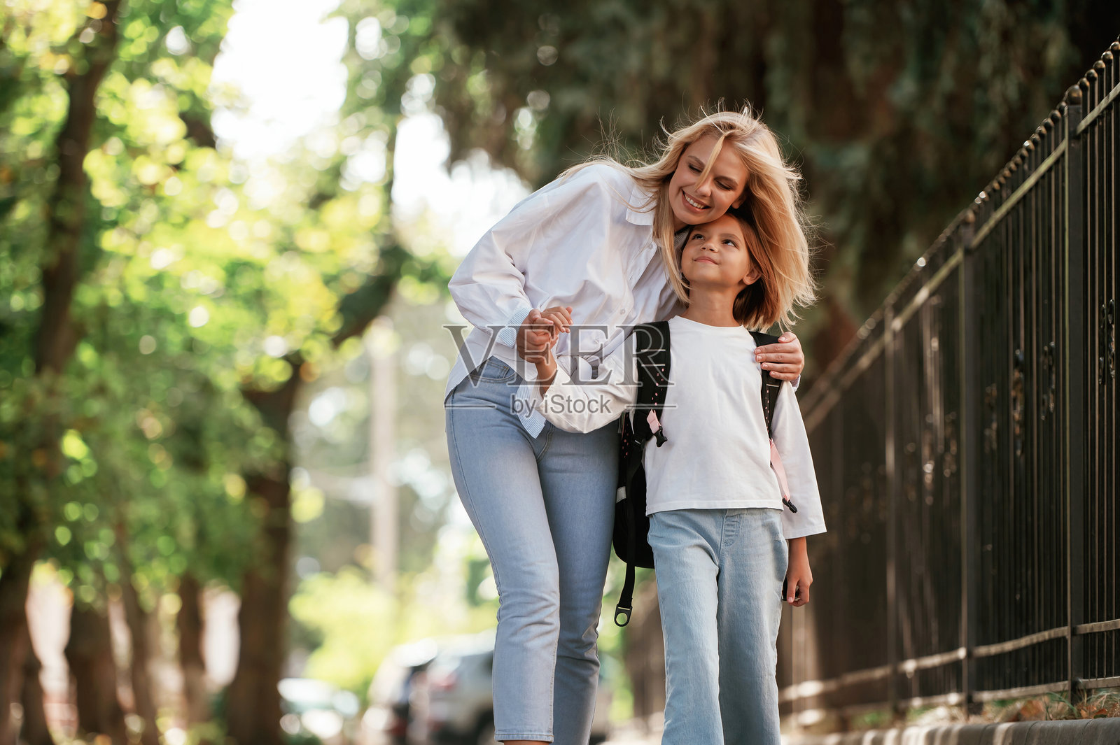 正面视角，走路。女学生与她的母亲在户外一起。照片摄影图片