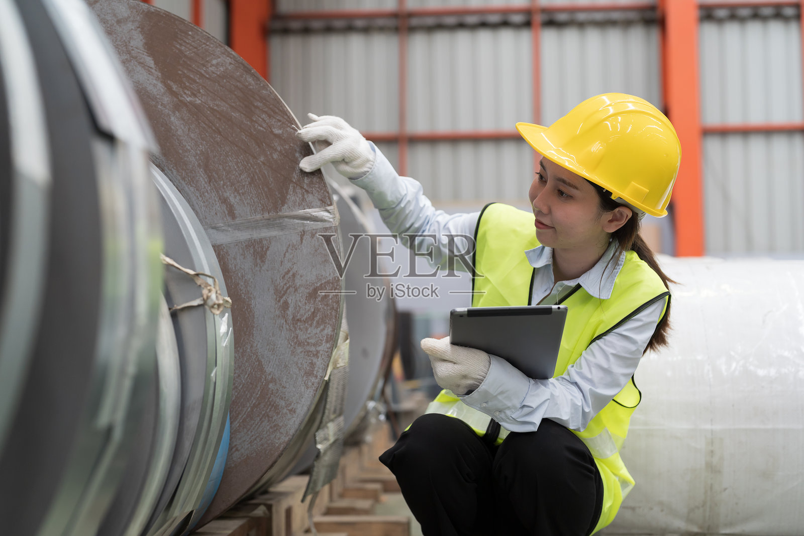 金属加工制造，原材料仓库。亚洲女性工人在检查镀锌或金属板的质量卷材。女性工人在不锈钢卷材仓库工作。照片摄影图片