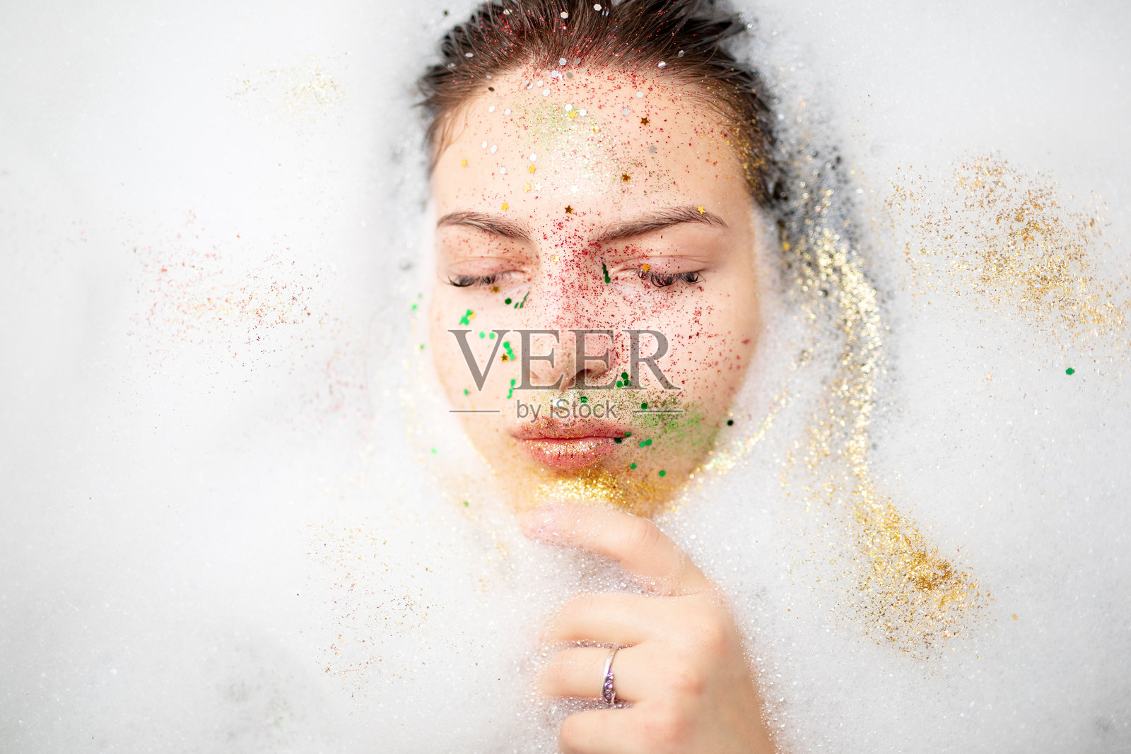 浴室中，年轻女性闭着眼睛，脸上闪烁着亮片。照片摄影图片