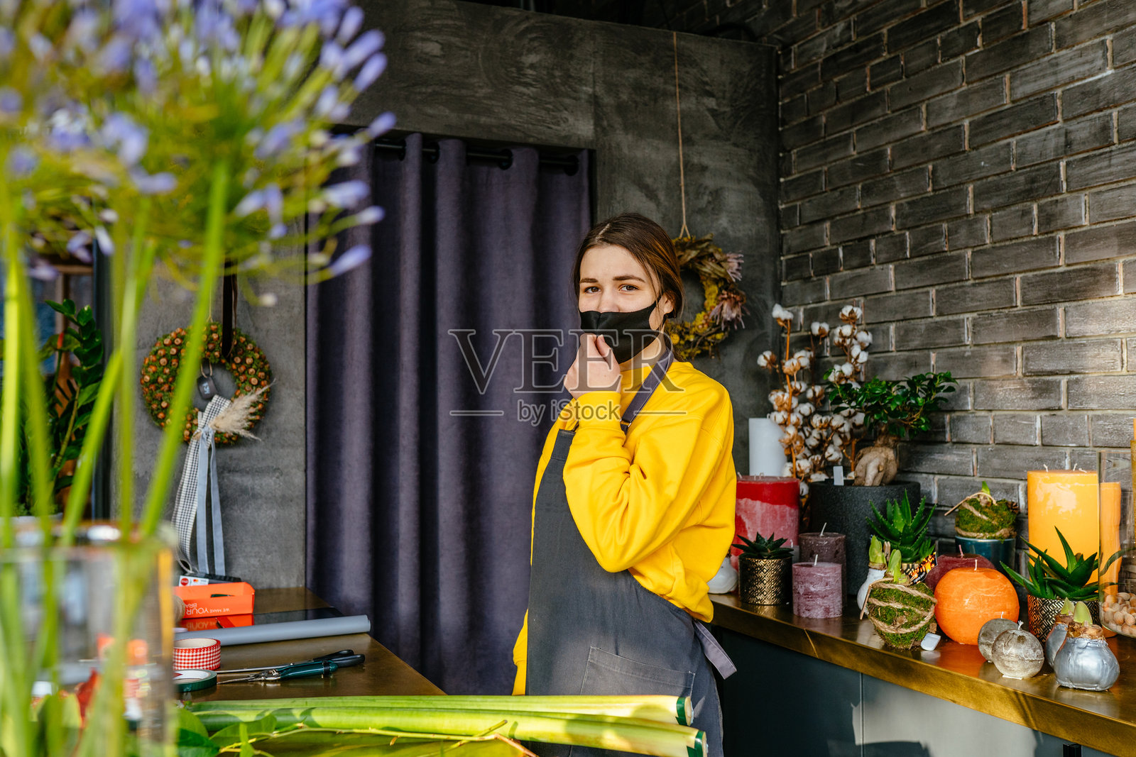 年轻女助理花店员佩戴防护口罩，身穿制服，在现代花卉和礼品店内工作。照片摄影图片
